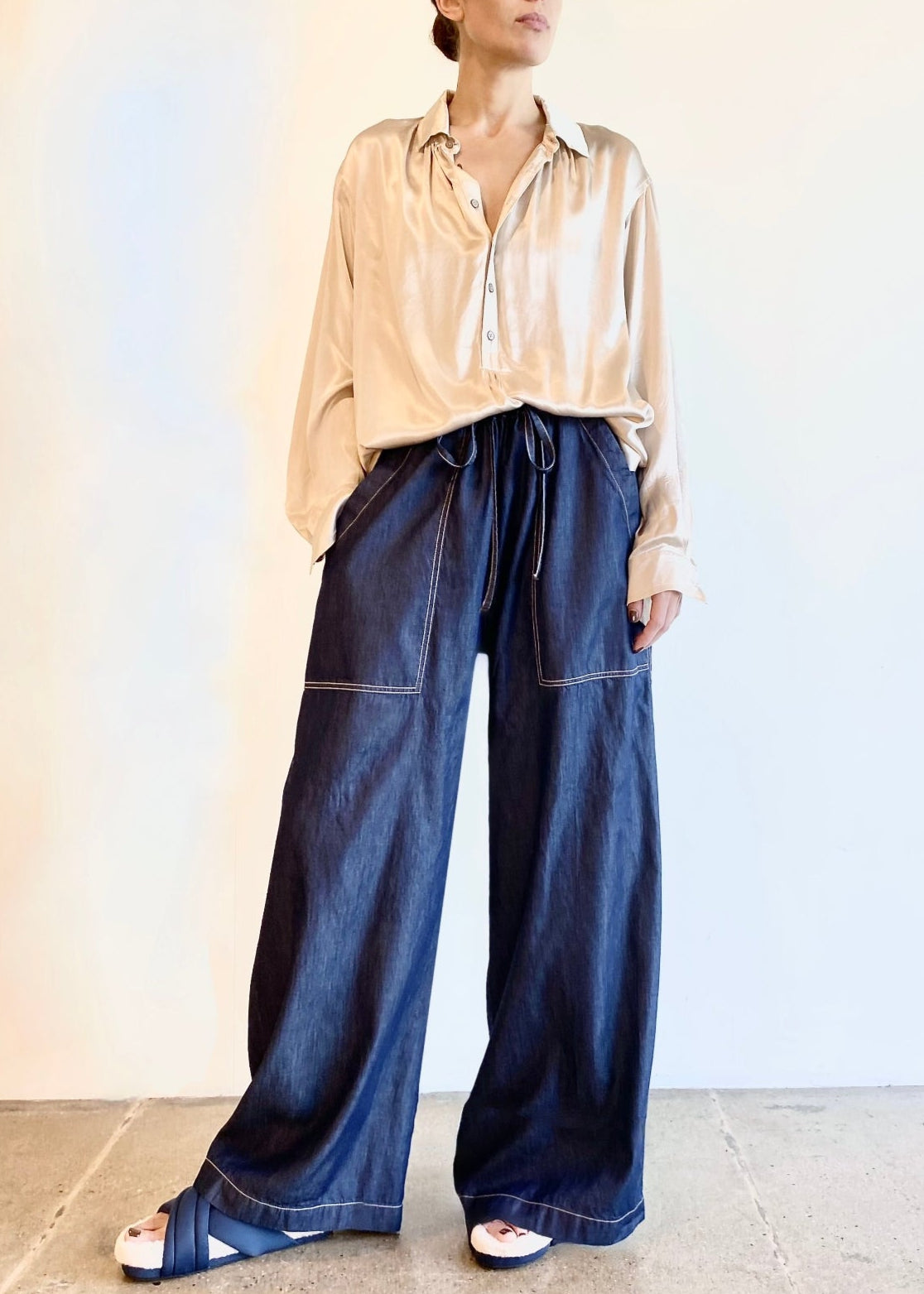 Woman wearing a beige Agnes blouse and blue wide-leg denim pants against a plain background