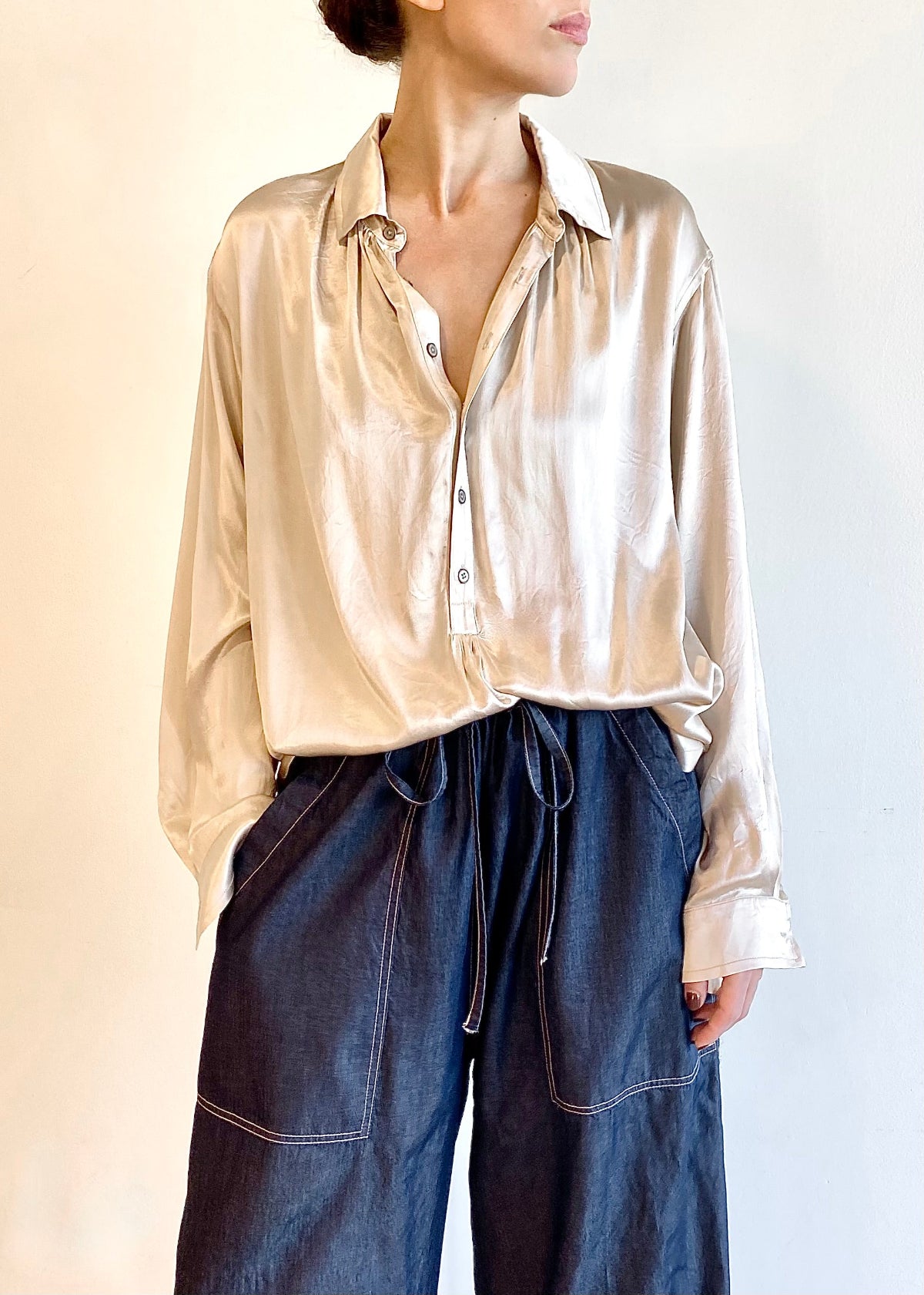 Person wearing a beige silk Agens button shirt and blue denim pants against a white background
