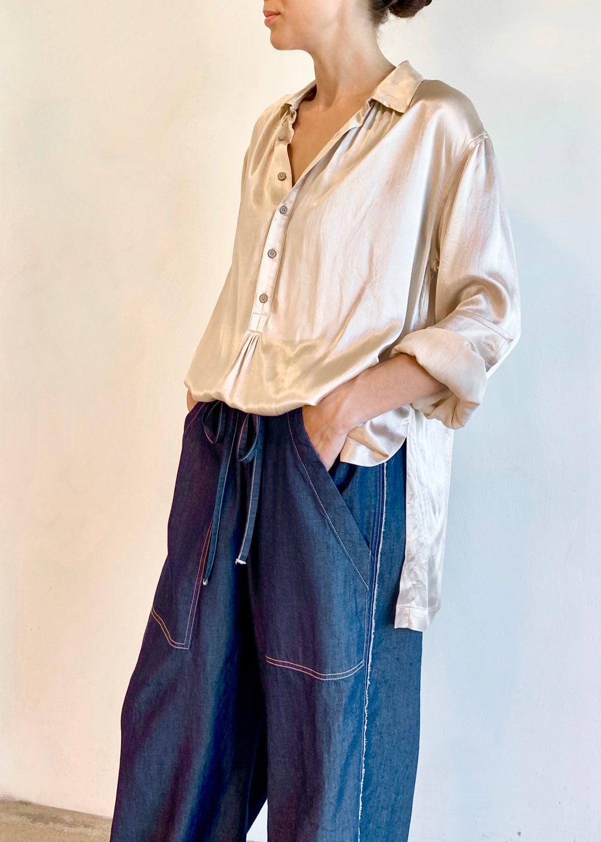 Person wearing a beige silk Agens button shirt and blue denim pants against a white background