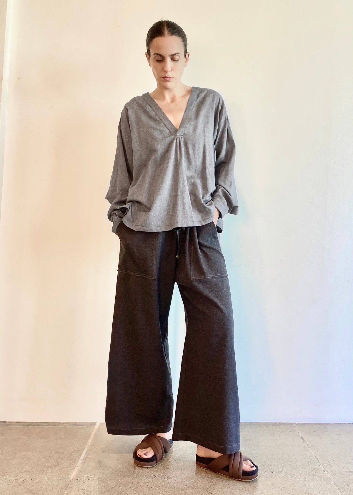 Woman wearing a gray Farmers Smock top and dark flannel pickers pants against a plain background