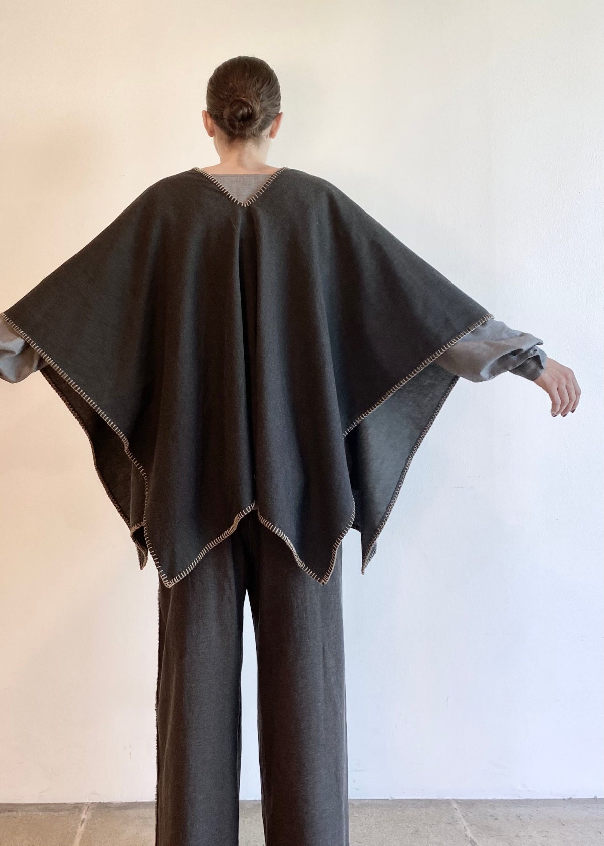 rear view of Person wearing a dark gray poncho over a matching gray pants outfit against a plain background