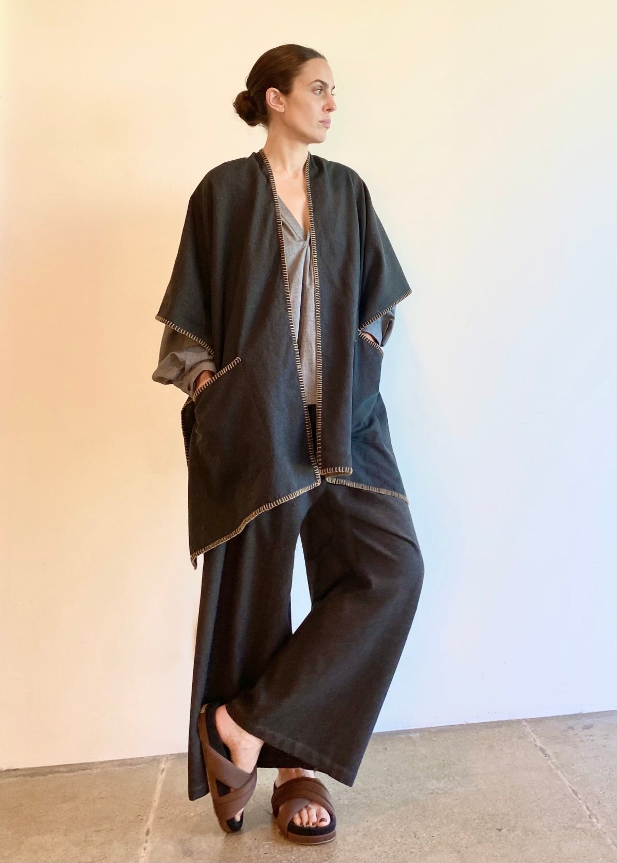 Woman wearing a dark gray poncho shawl over a light gray top and pants on a white background