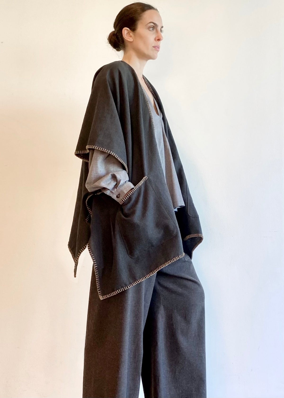Woman wearing a dark gray poncho shawl over a light gray top and pants on a white background