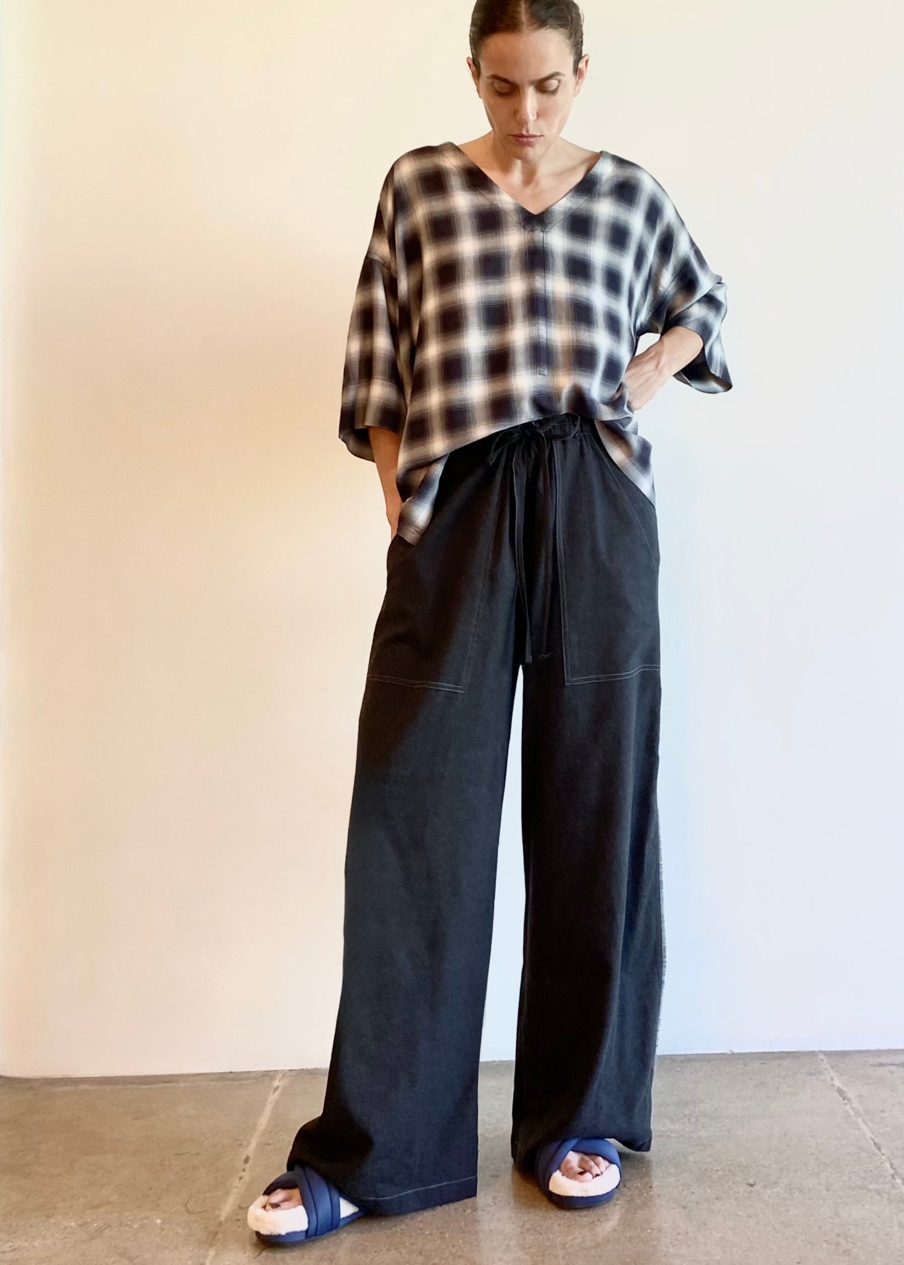 Person wearing a plaid shirt and wide-leg pants against a plain background