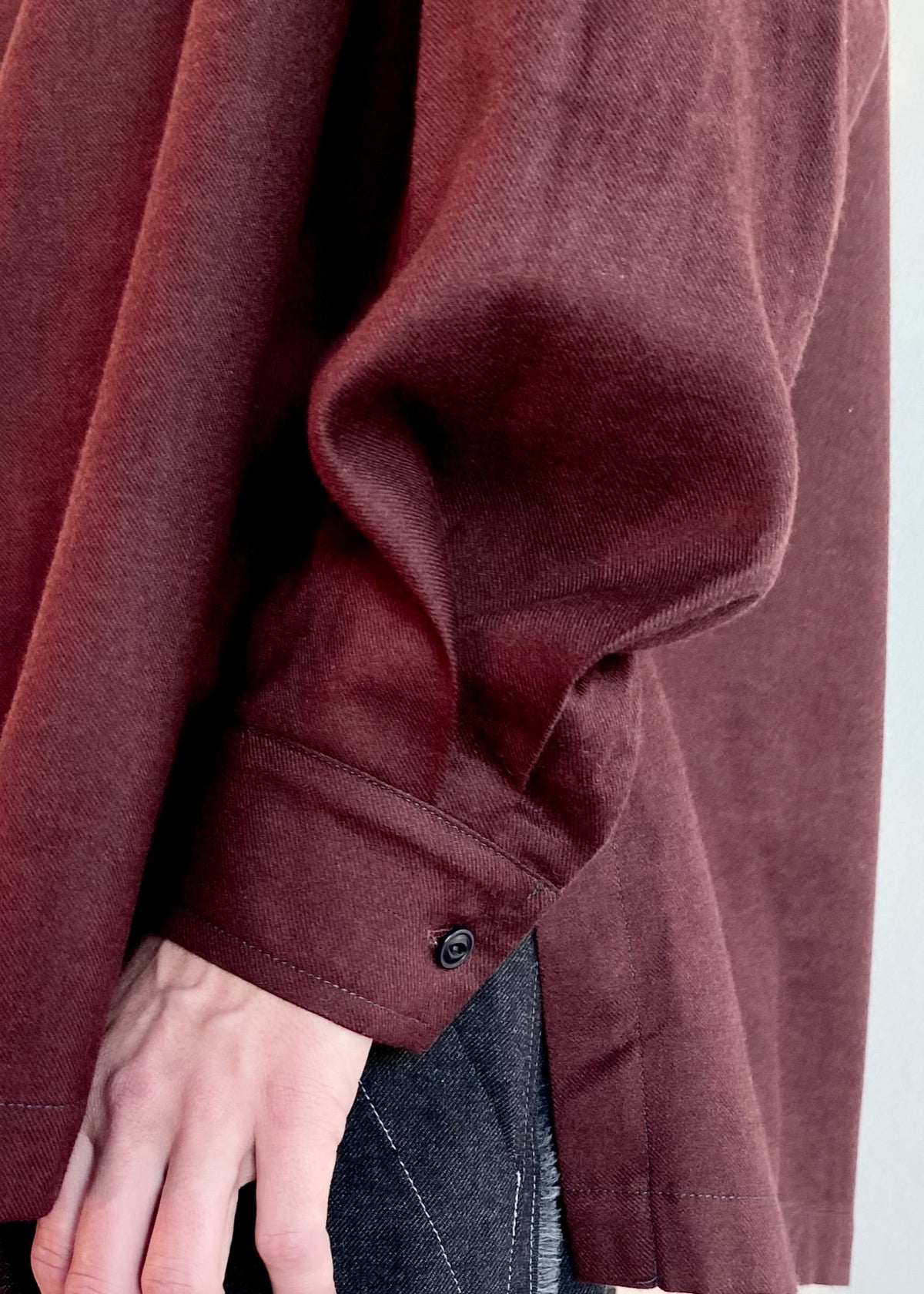 Close-up of a person's sleeve cuff of a burgundy shirt with a white background