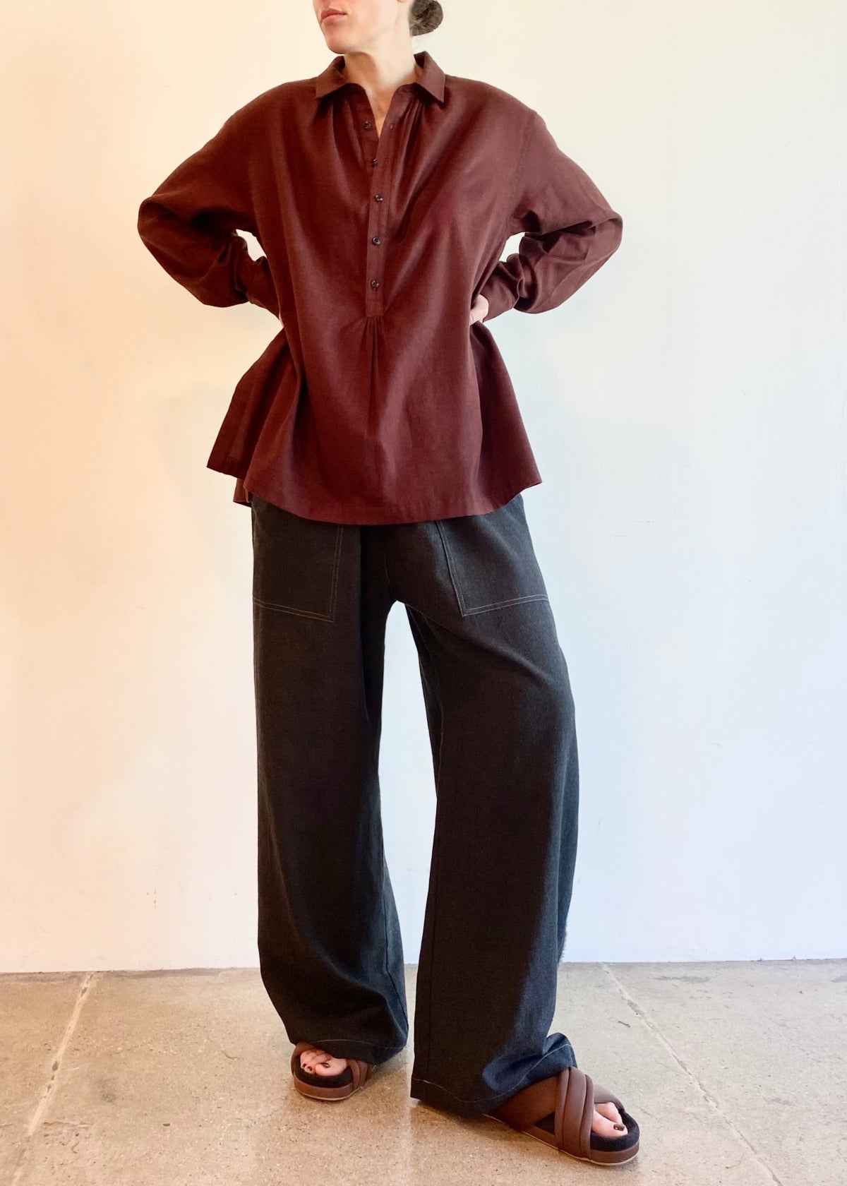 Woman wearing a burgundy blouse and dark gray pants against a plain background