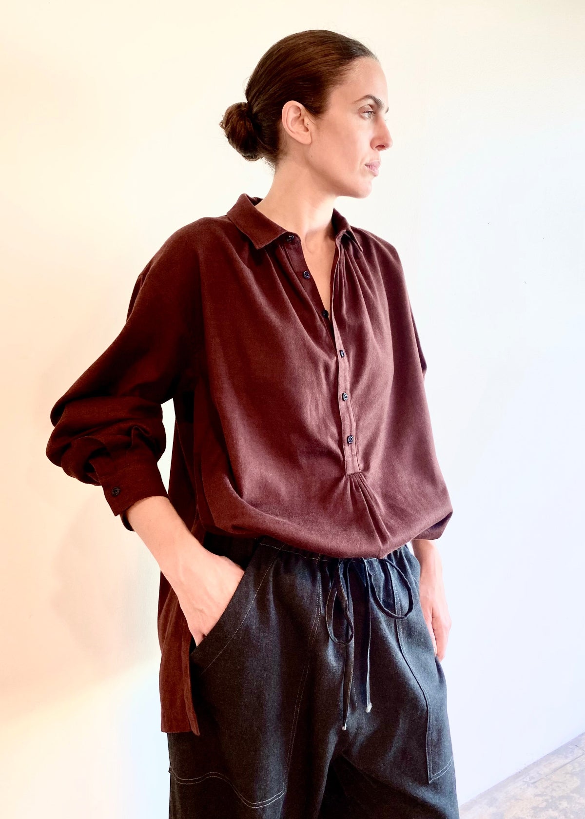 Woman wearing a burgundy blouse and dark gray pants against a plain background