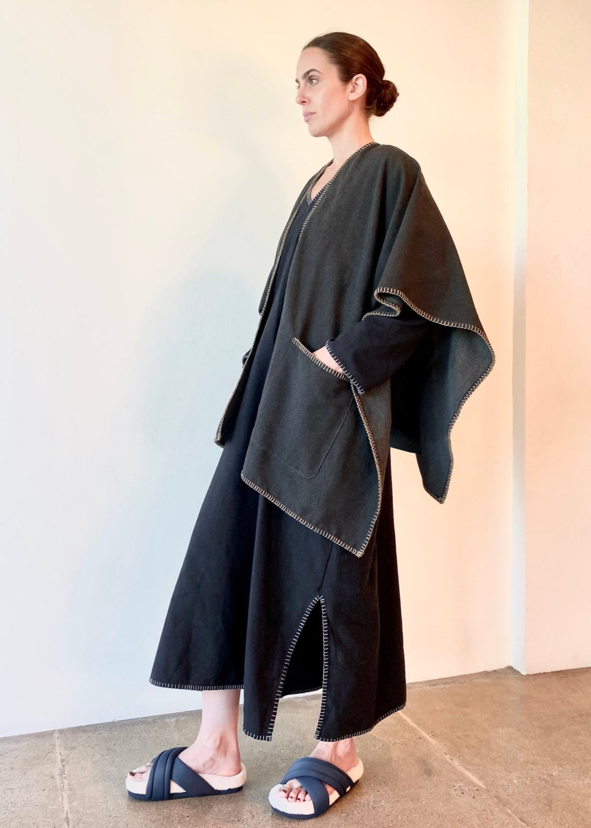 Woman wearing a dark gray Harvest poncho shawl over a black dress against a plain background