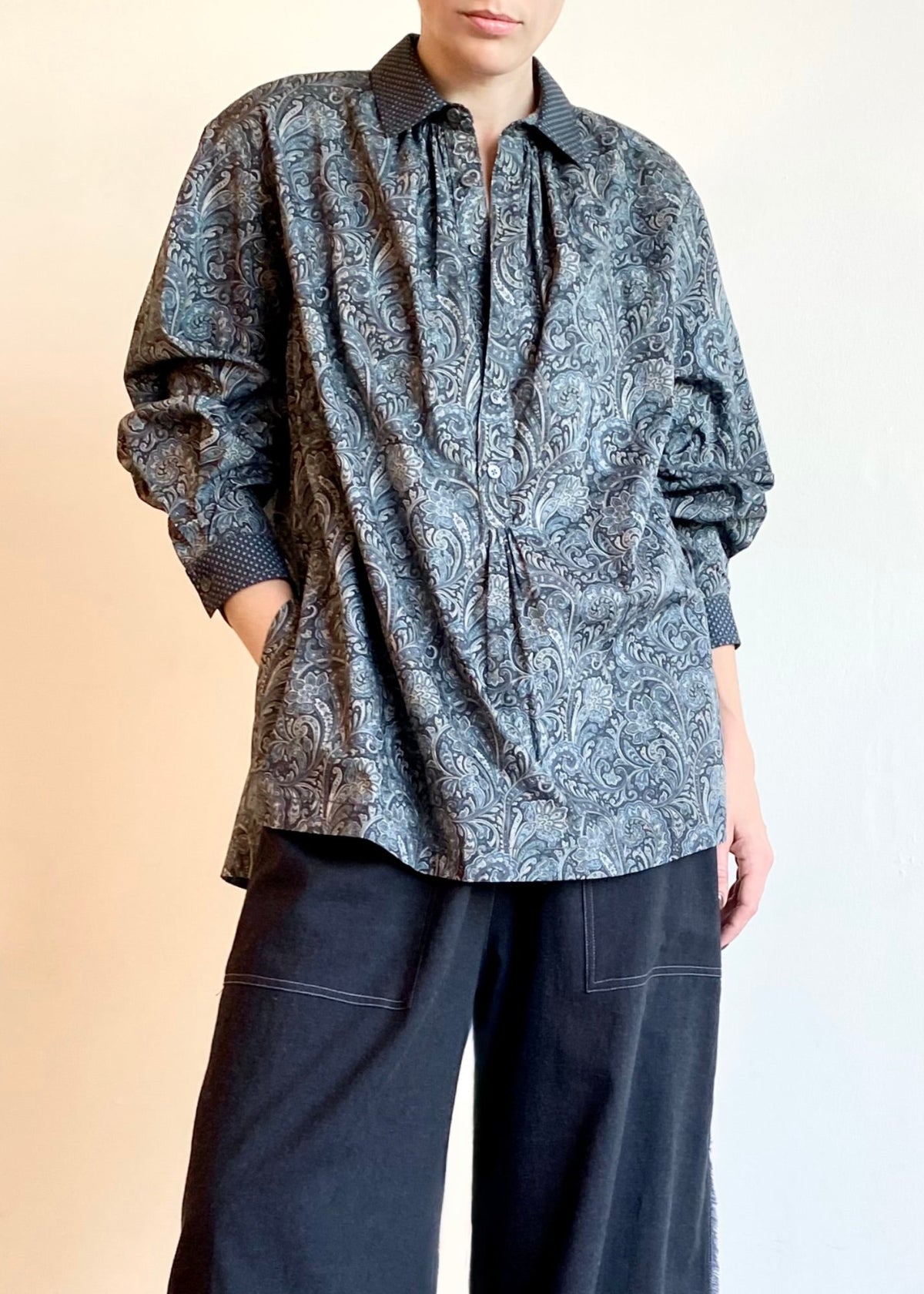 Person wearing a paisley patterned Agnes shirt and dark gray pants on a neutral background