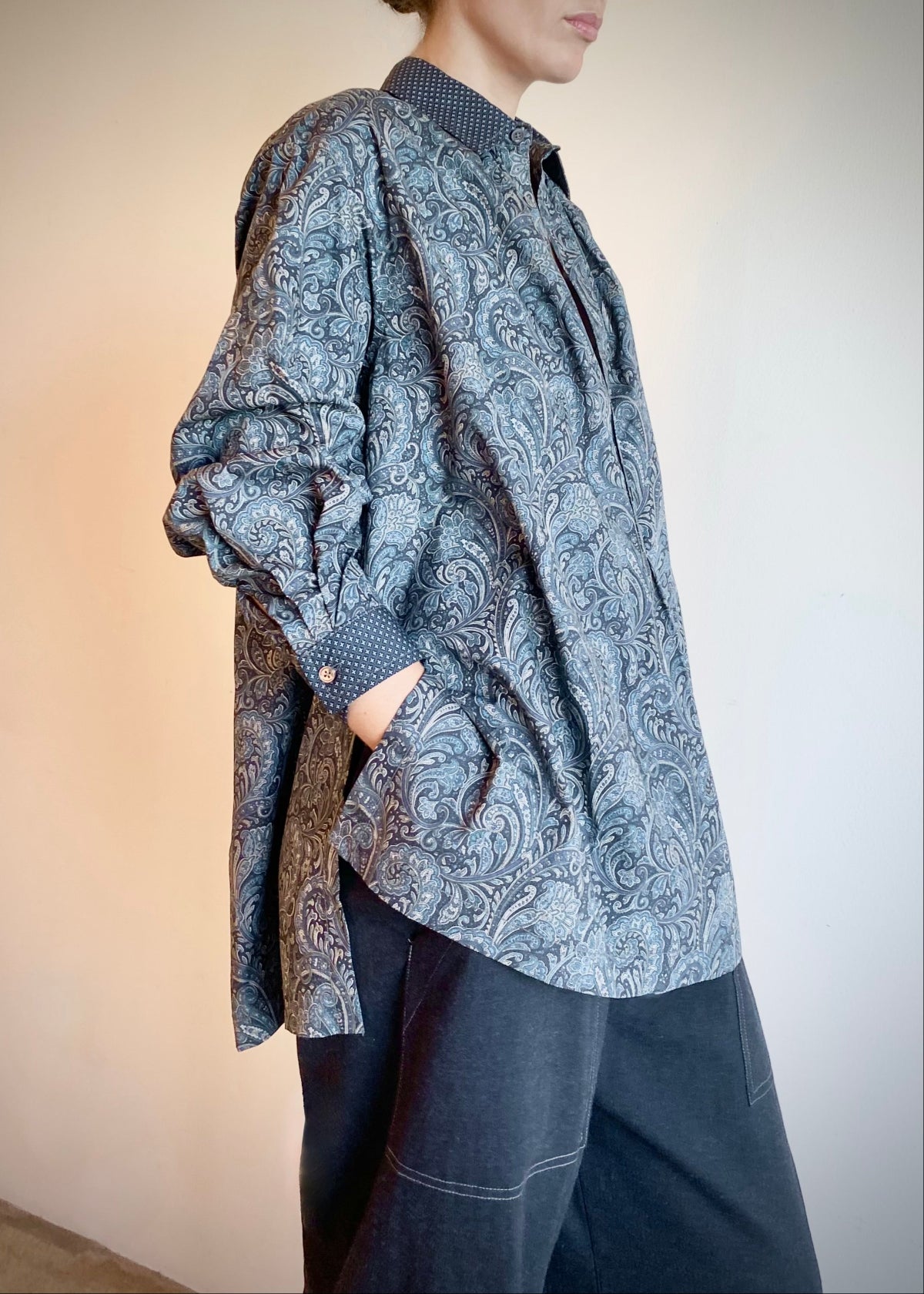 Person wearing a paisley patterned Agnes shirt and dark gray pants on a neutral background