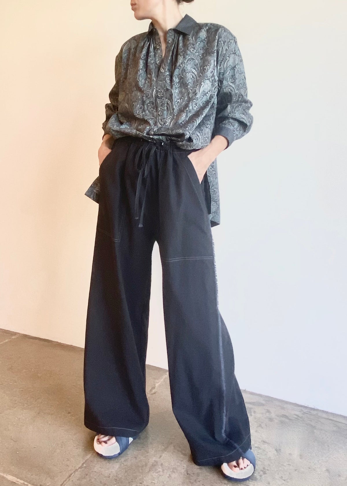 Person wearing a paisley patterned Agnes shirt tucked into dark gray pants on a neutral background