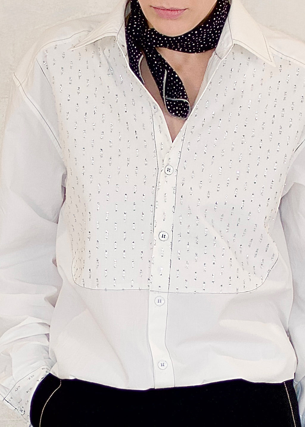 Person wearing a white blouse with silver metalic details against a plain background