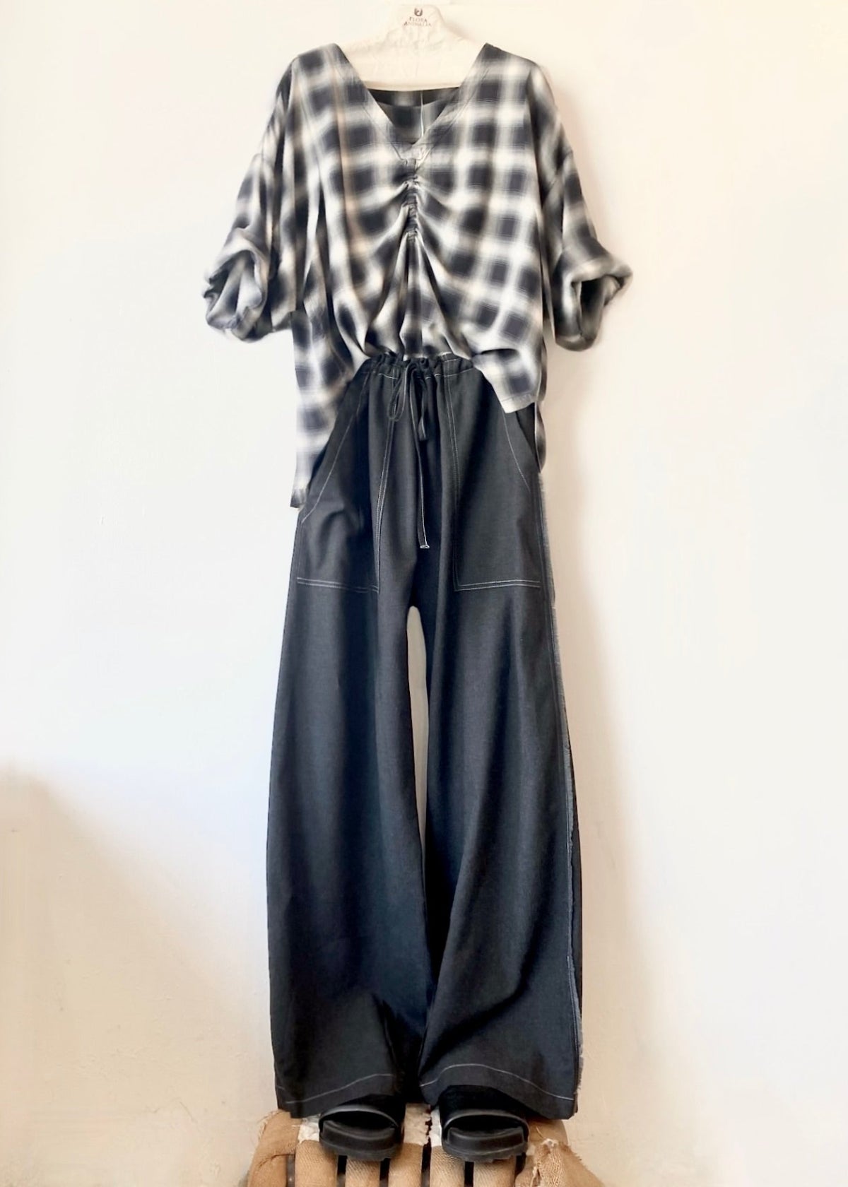 extra long dark drawstring pants and plaid top hanging against a white wall