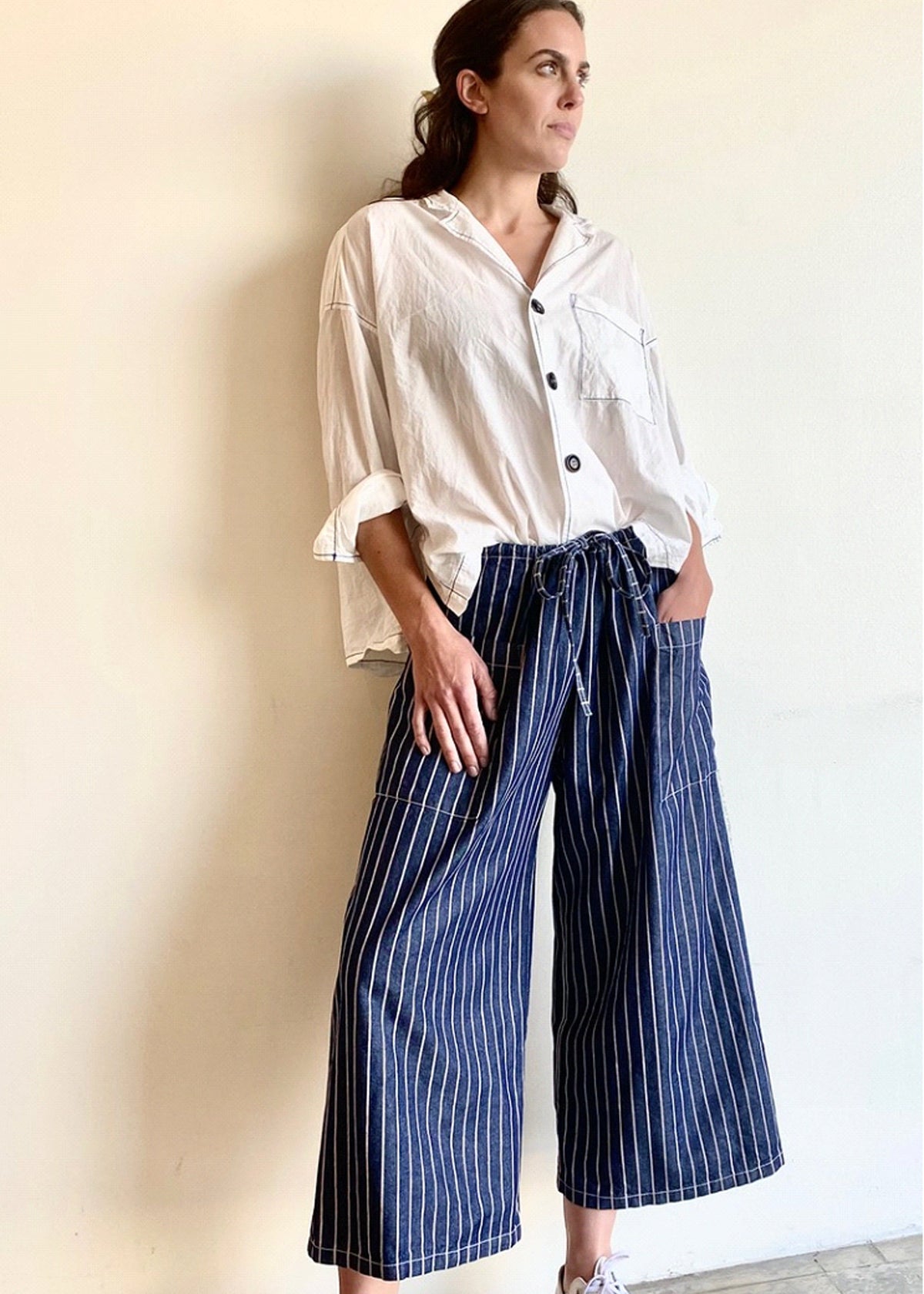 blue and white striped denim cropped drawstring pants with white button down top. Hand in pocket