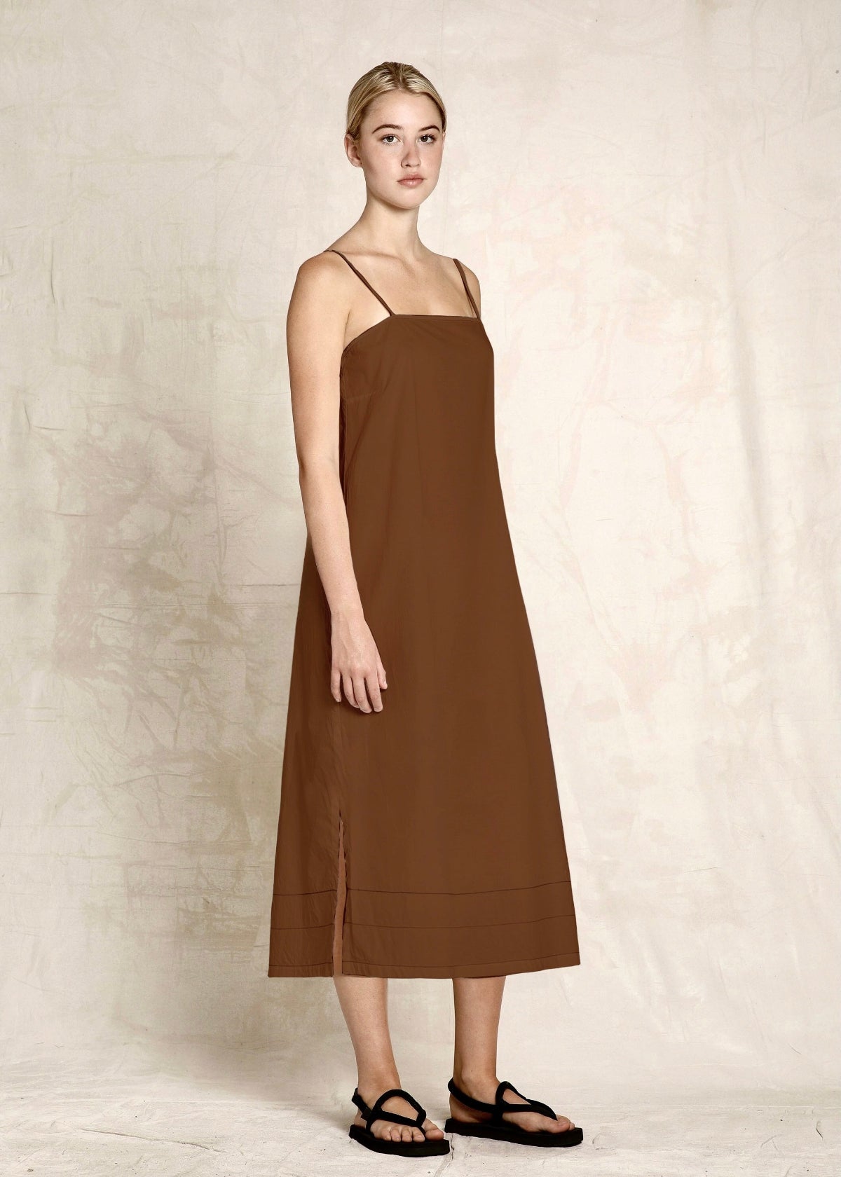 Woman wearing a brown slip dress against a plain background