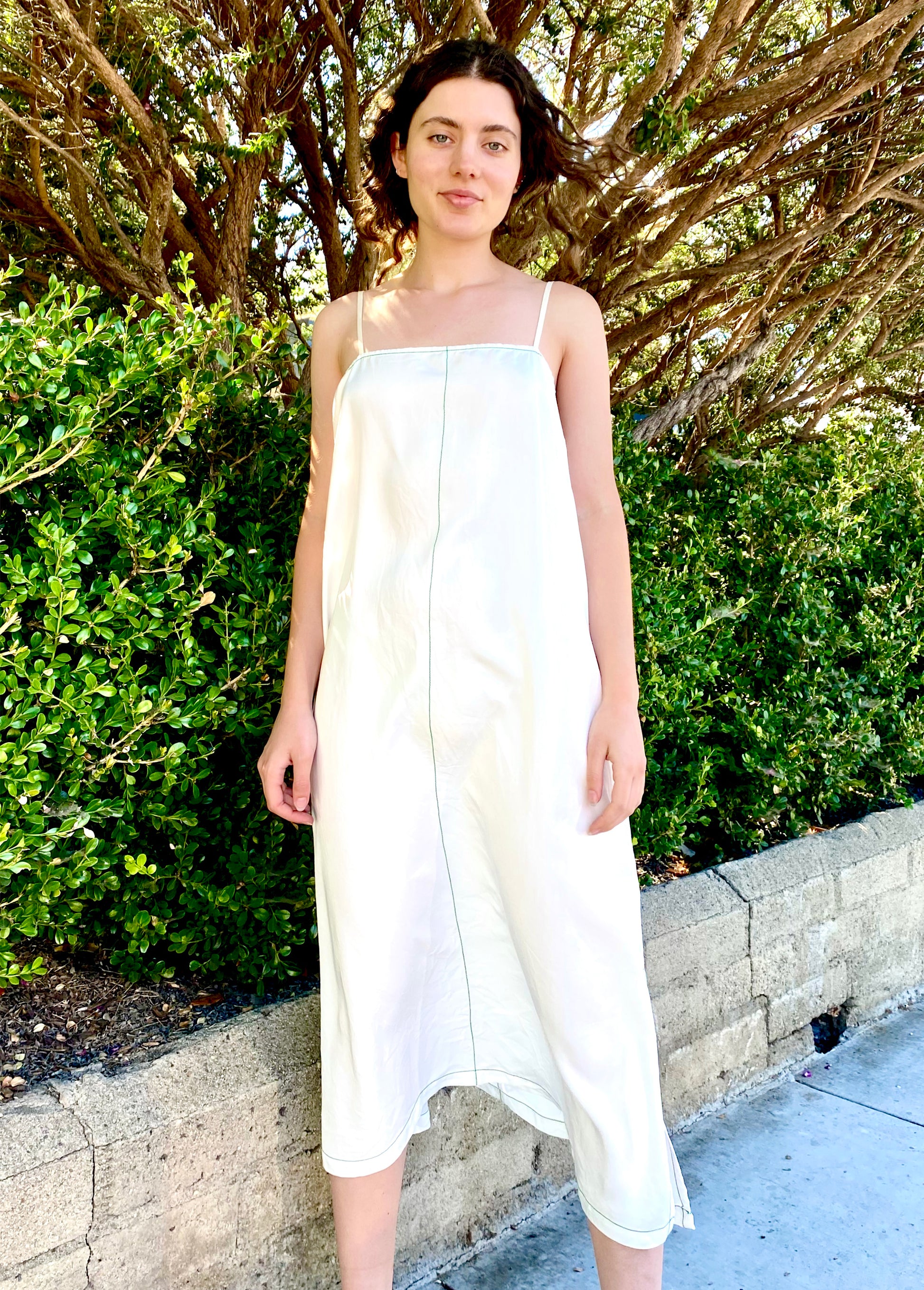 white spaghetti strap dress on model outside against a green bush