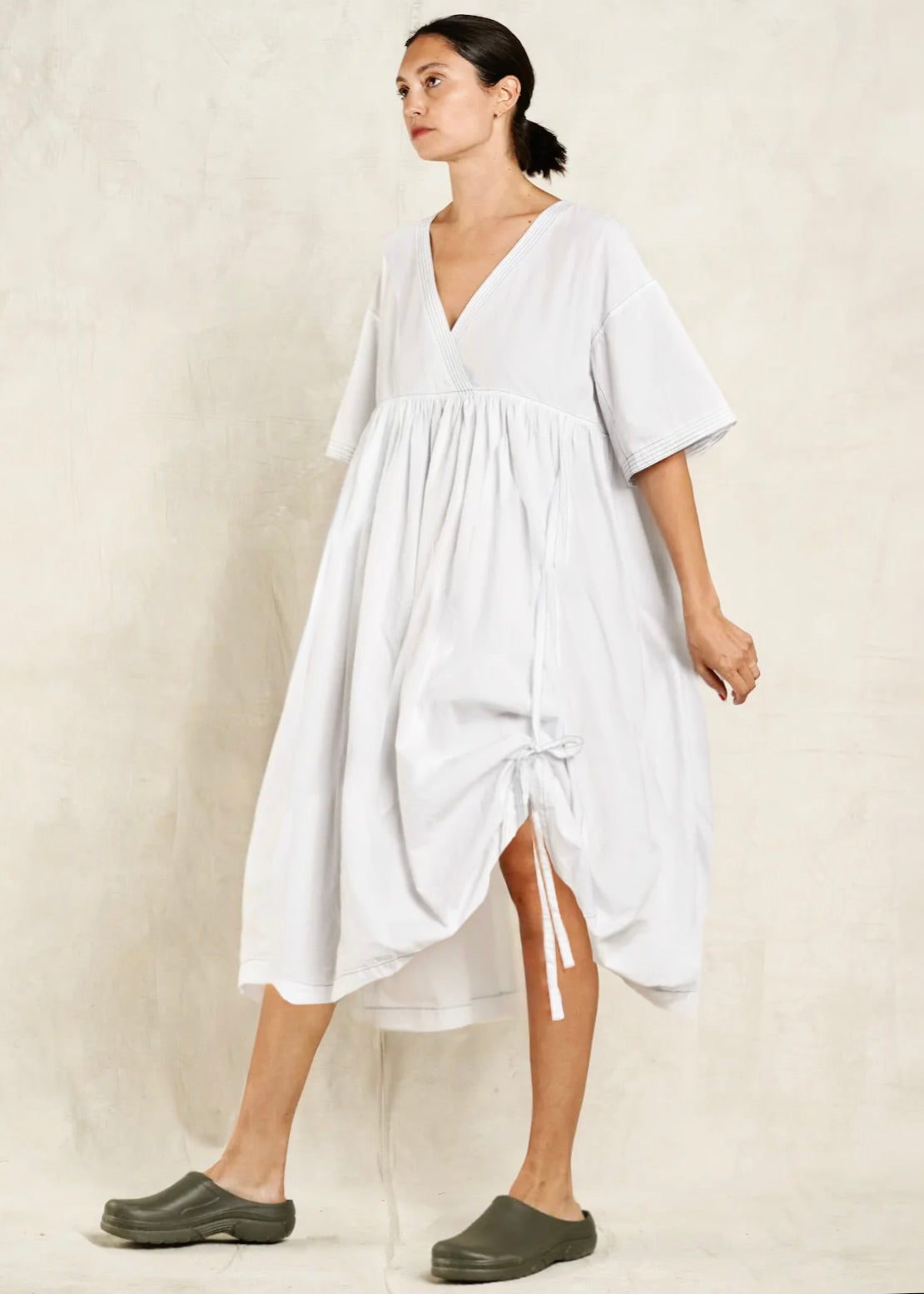 Woman wearing a white dress with cinched hem and a plain background