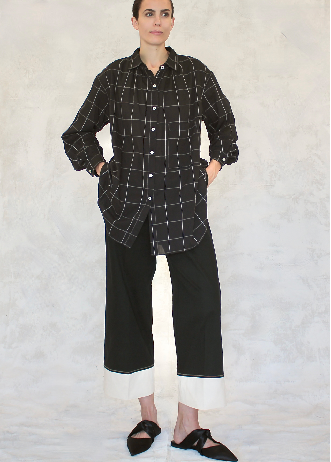 A person wearing a classic black and white checkered artist shirt with a collar, two front pockets, and button front placket.