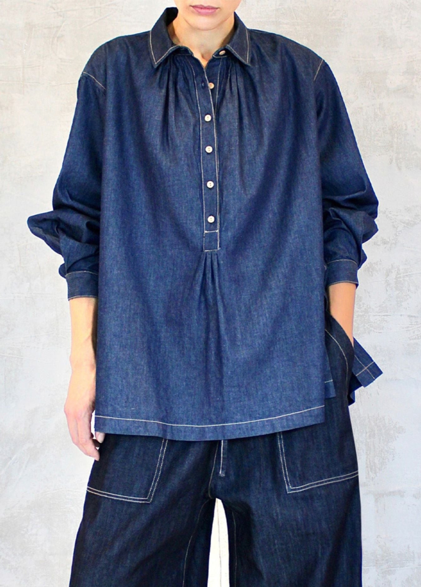 A person wearing a long-sleeved, button-up denim shirt with a classic collar, in a blue color, against a white background.