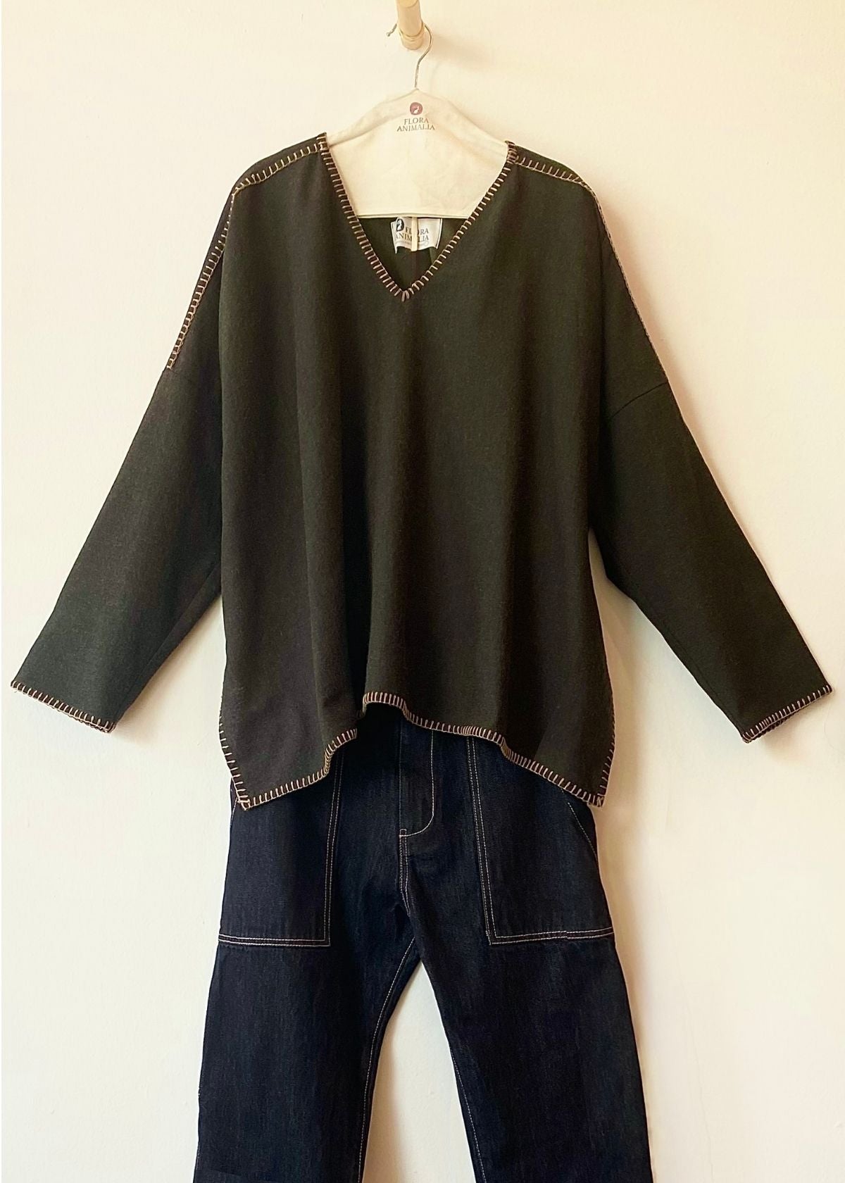 dark olive green v-neck Praia top with tan trim on a hanger against a white background