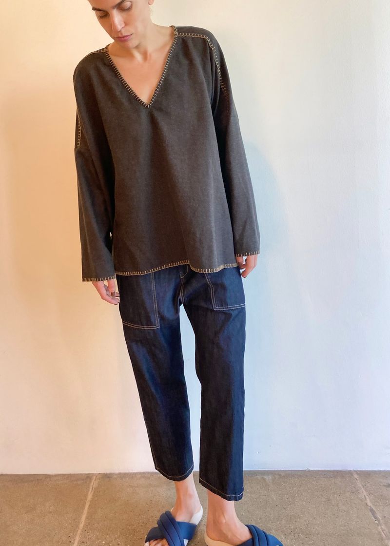 Person wearing a dark gray long-sleeve vneck Praia top and blue jeans against a neutral background