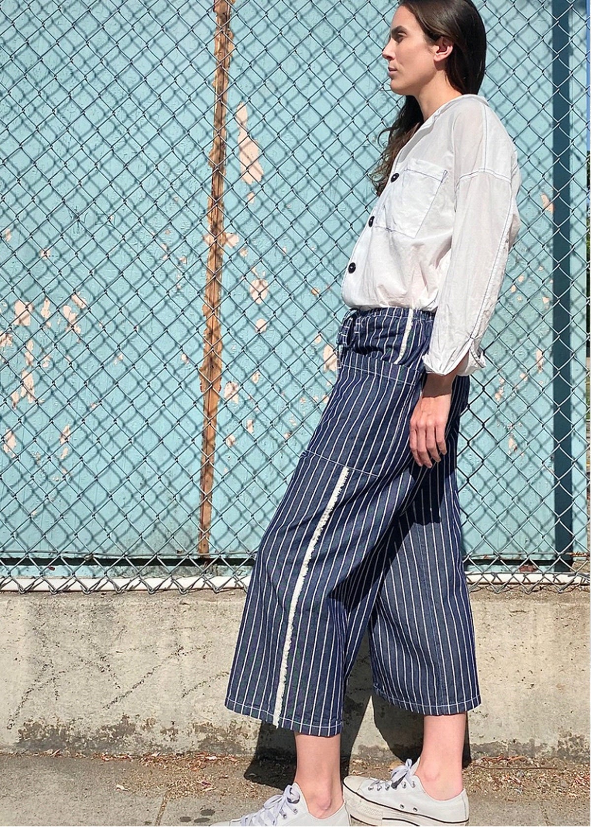 blue and white striped denim cropped drawstring pants with white button down top. side view