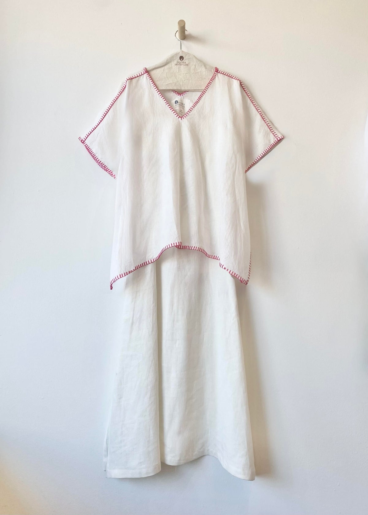 White top over white dress with pink trim on a hanger against a white background