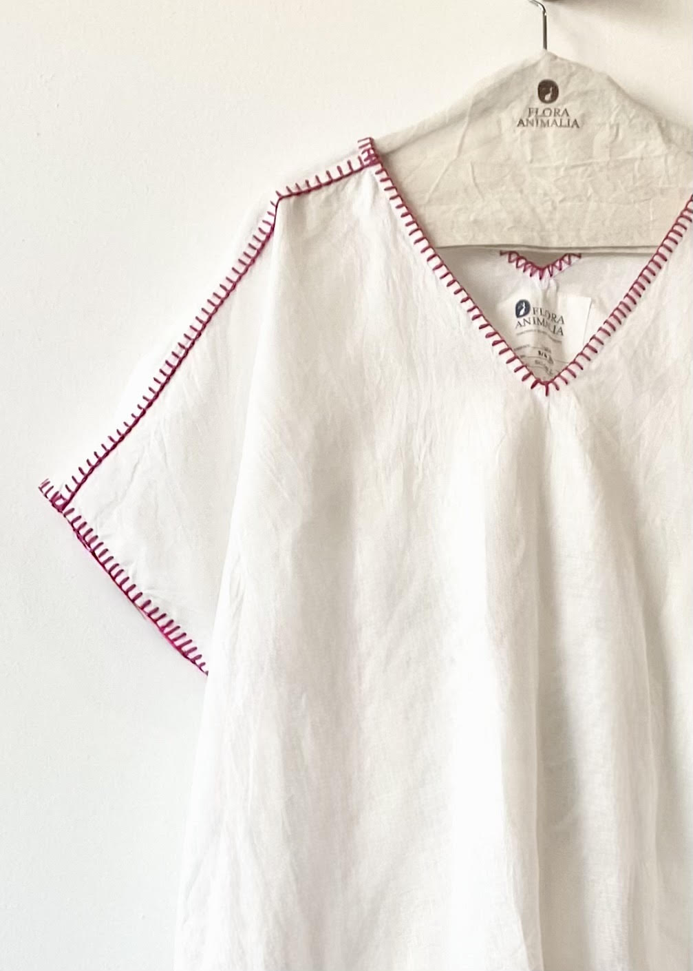 White shirt with fuchsia stitching on a hanger against a white background