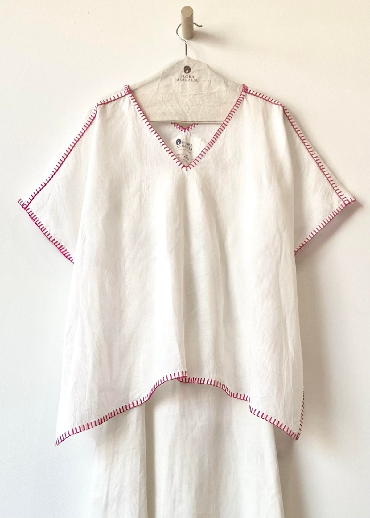 White top with red trim hanging on a wooden hook against a white background