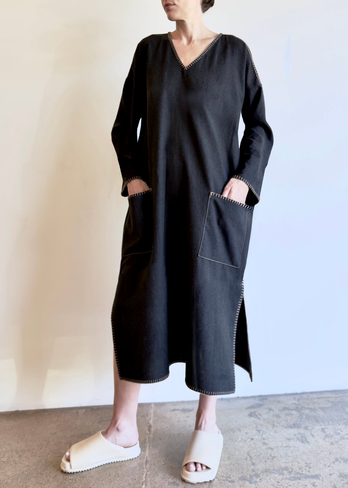 Person wearing a dark gray dress with pockets against a plain background