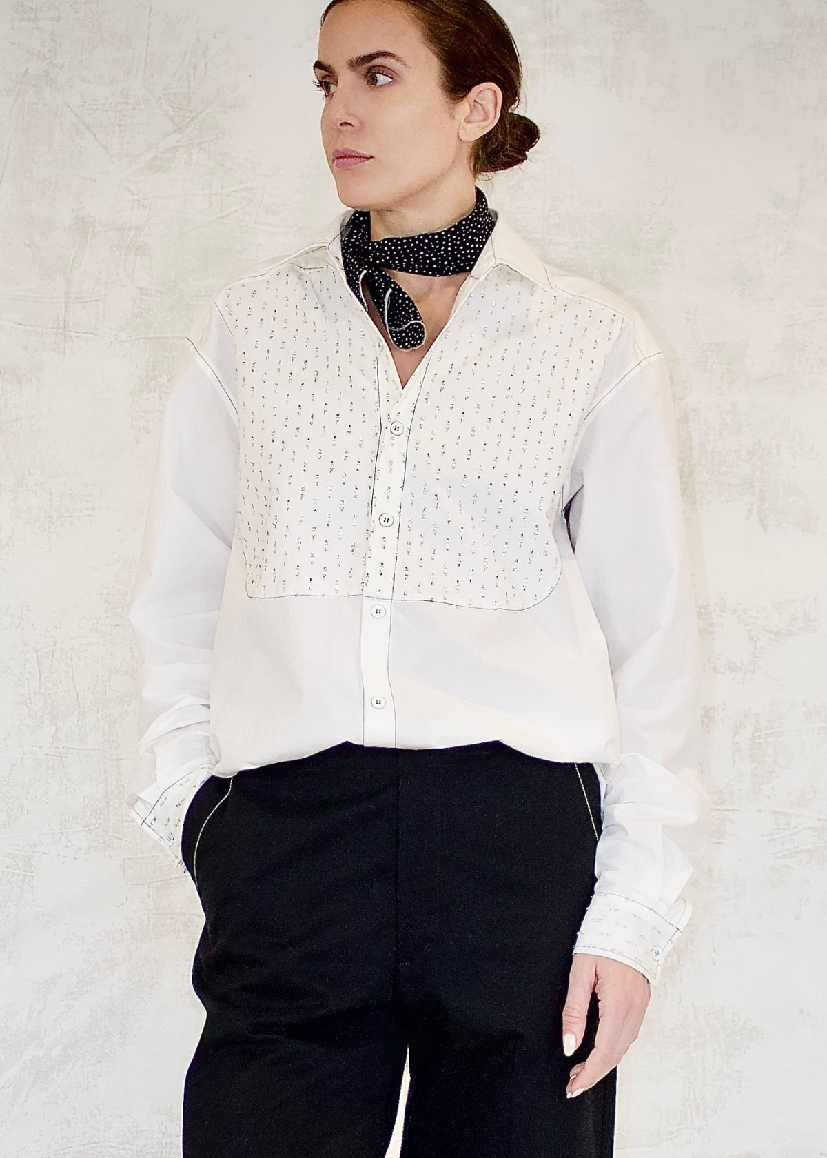 Person wearing a white blouse with silver detailing and black pants against a light background