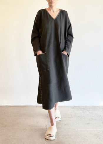 Person wearing a dark gray dress with hands in pockets against a plain background