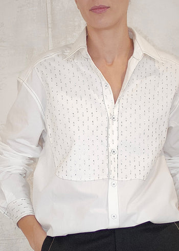 Person wearing a button up white blouse with silver metallic details against a plain background