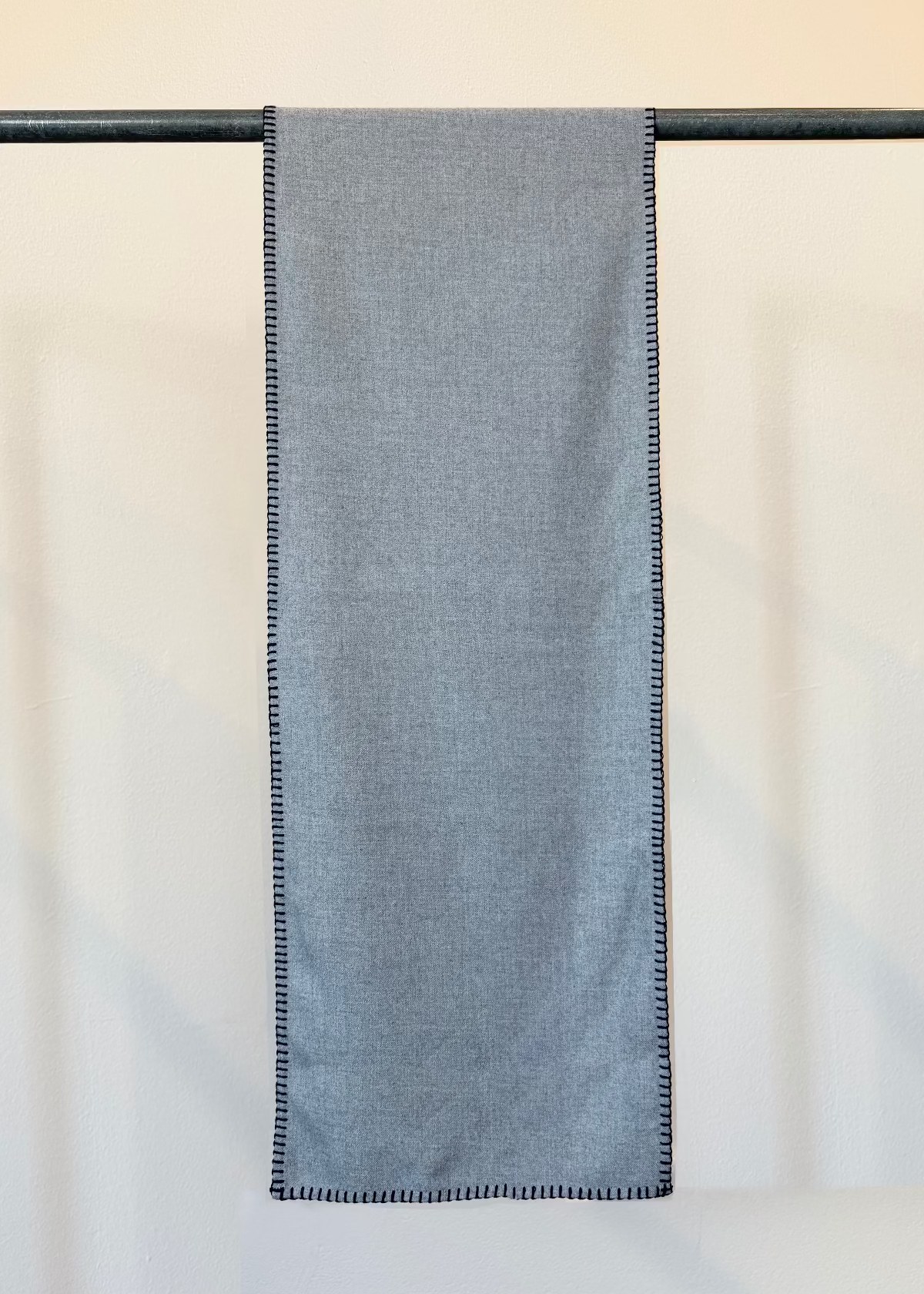 Everyday Scarf in Ash Gray Plant based flannel with blanket edge stitch hanging flat from a pole against a plain background.