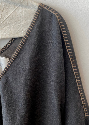 Shoulder-v-neck of dark gray top with light brown stitching on a textured white background