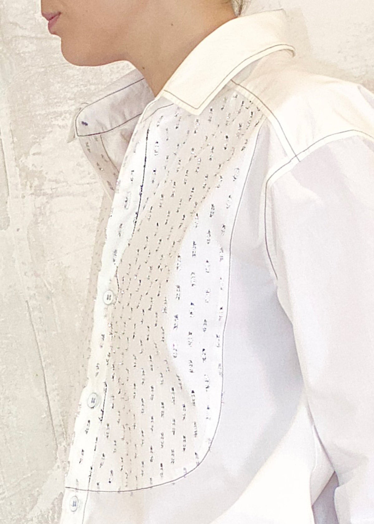 Close-up of a white shirt with silver metallic dots on a neutral background