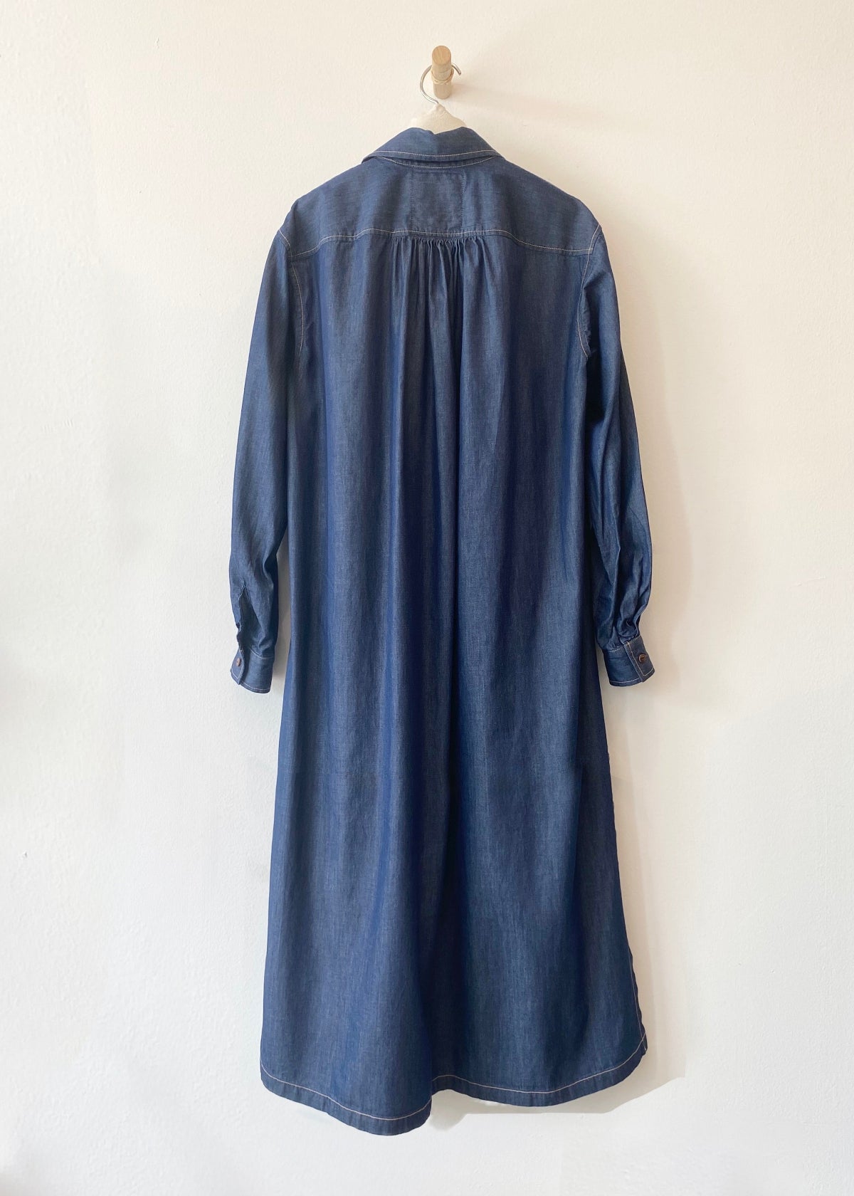 back of Blue denim Agnes dress on a hanger against a white background