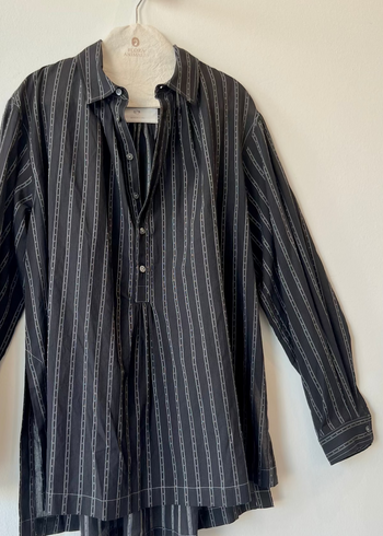 black shirt with white stripes and unbuttoned collar hanging against white wall