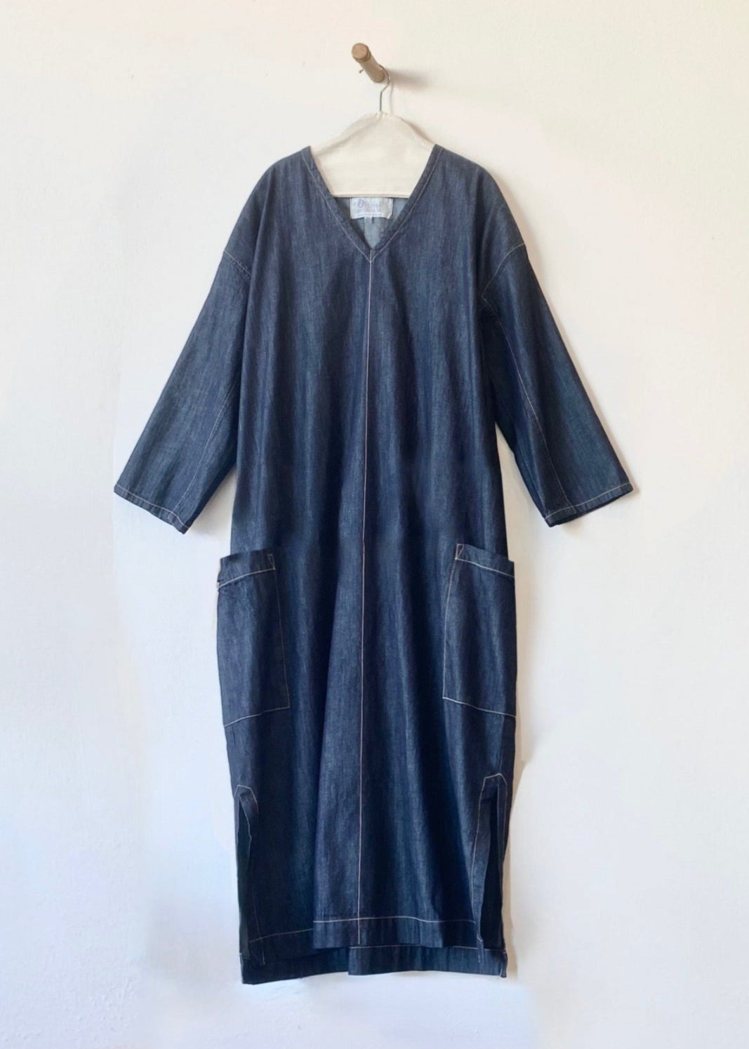 Blue denim lanatus dress on a hanger against a white background