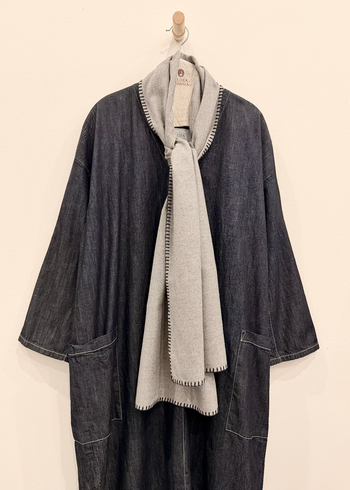 Denim Latatus Dress with Everyday Scarf in Ash Flannel tied at the neckline, hanging against a white wall.