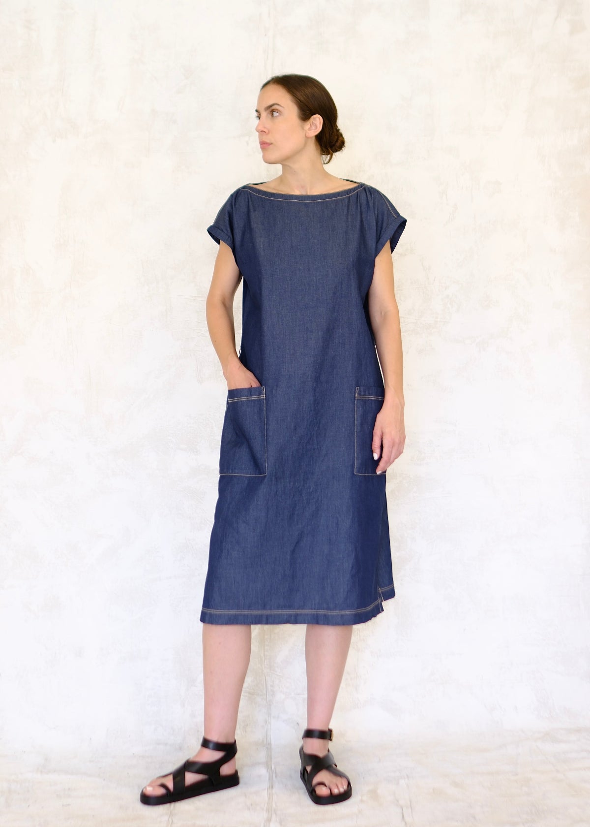 model in belted denim boat neck dress with hand in pocket
