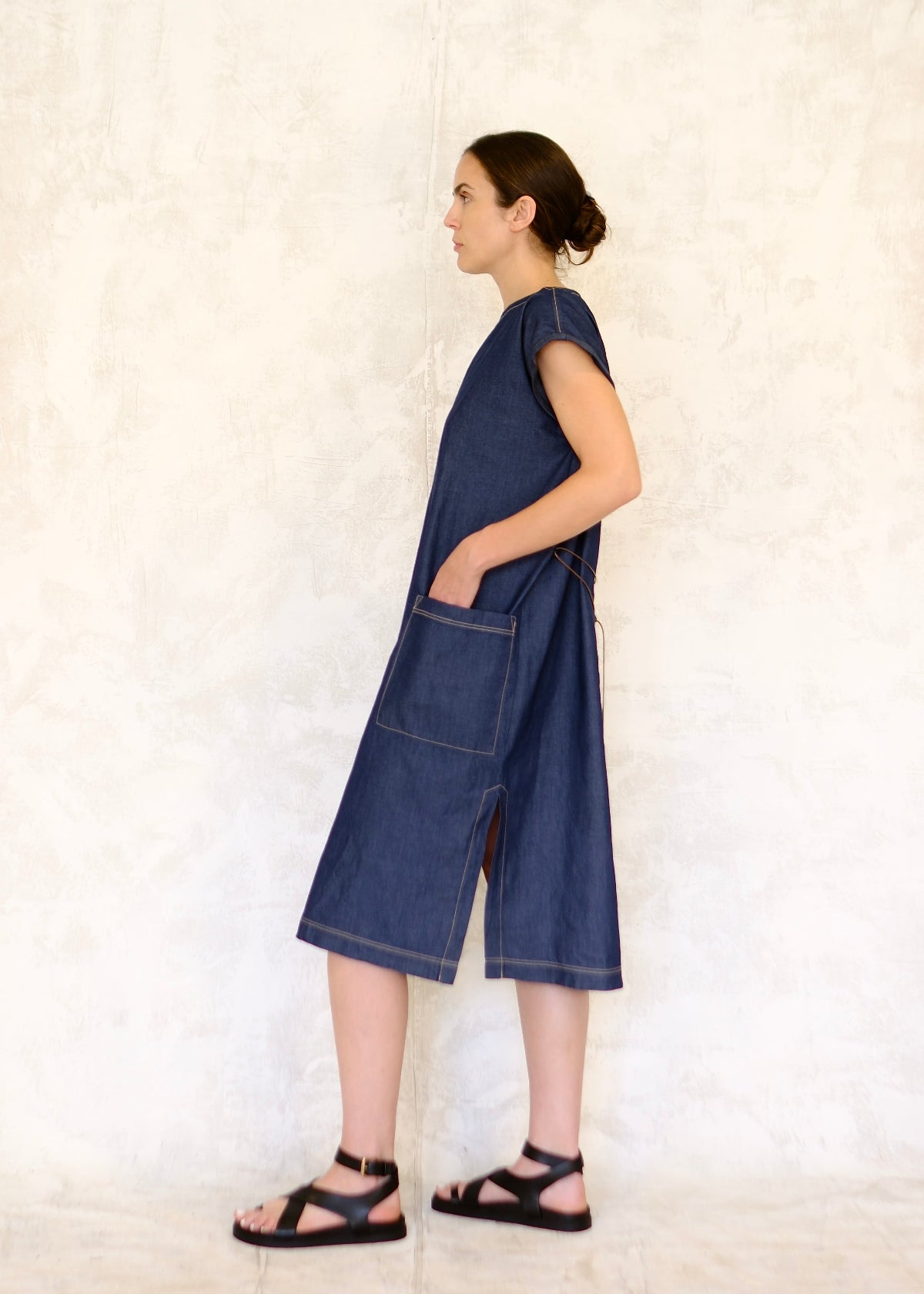 model in belted denim boat neck dress with hand in pocket