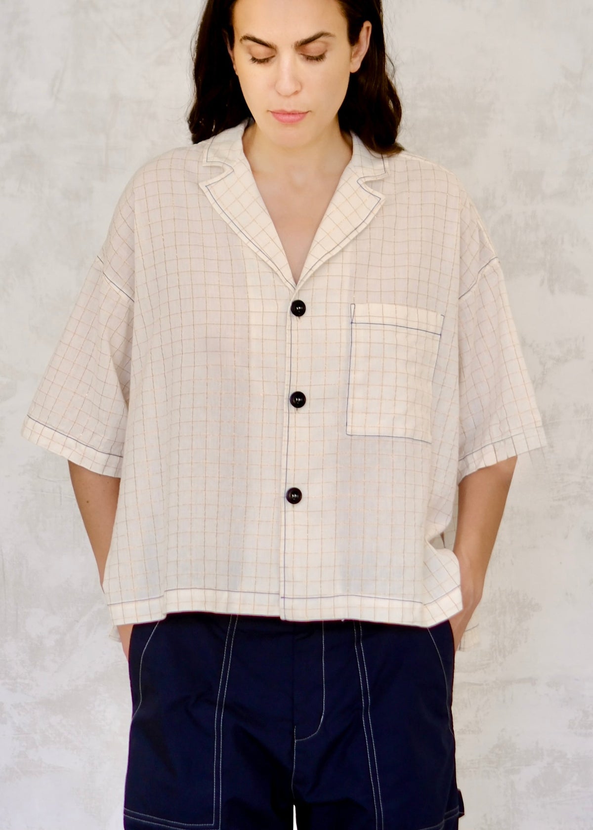 Woman wearing a cream checkered shirt with black buttons on a light gray background