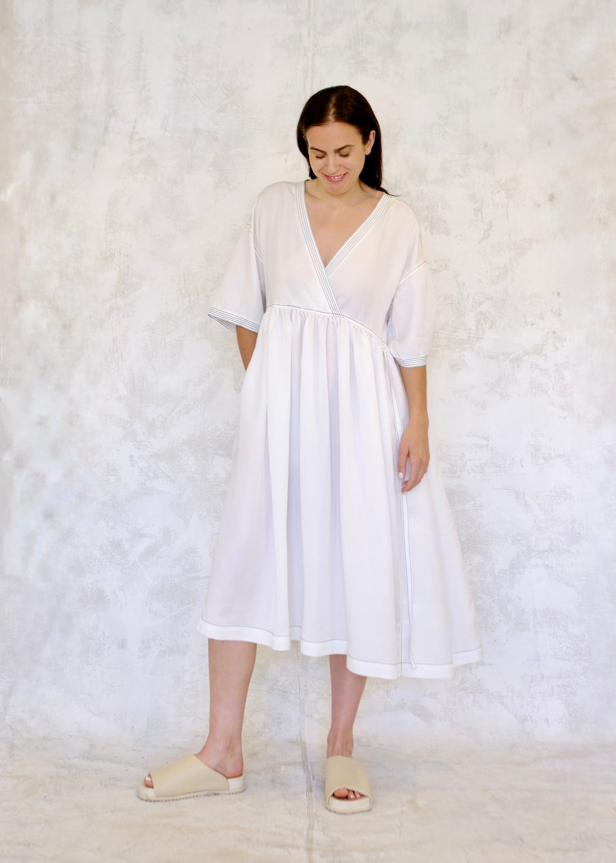 Woman wearing a white v-neck empire waiste dress against a white background