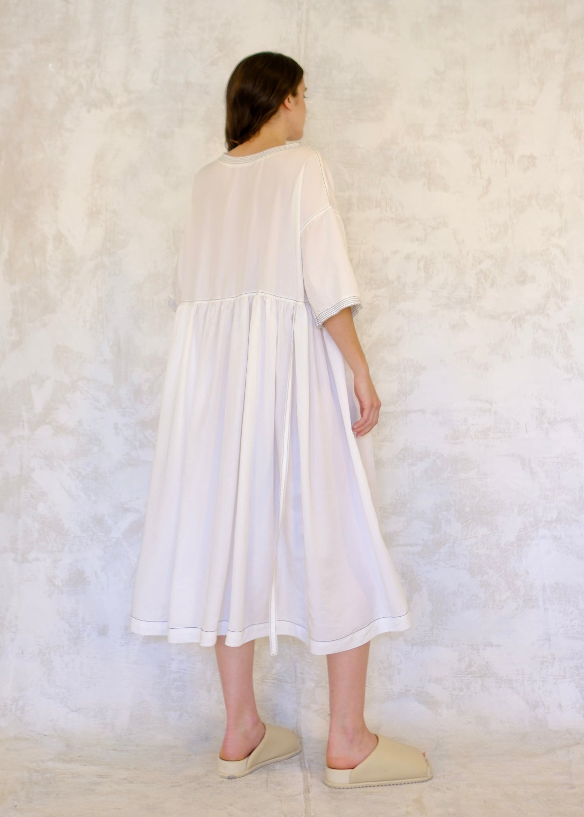 Rear view, Person wearing a white dress against a textured white background