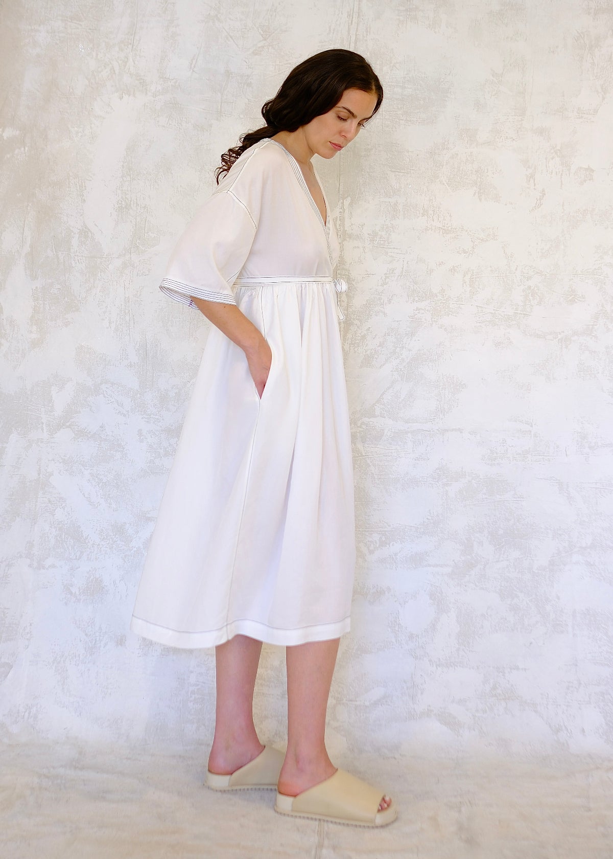 Woman wearing a white dress, wide sleeves to elbows, against a textured white background