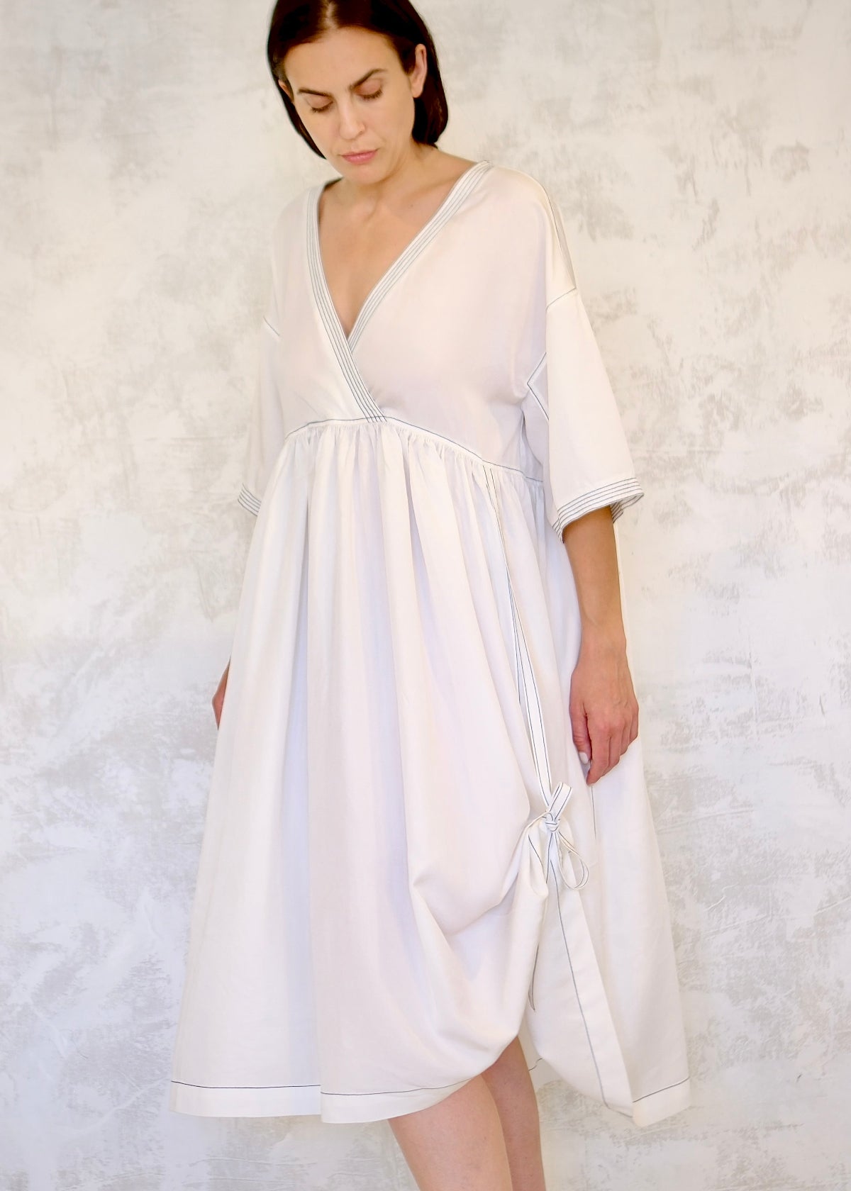 Woman wearing a white dress with tied hem against a textured white background