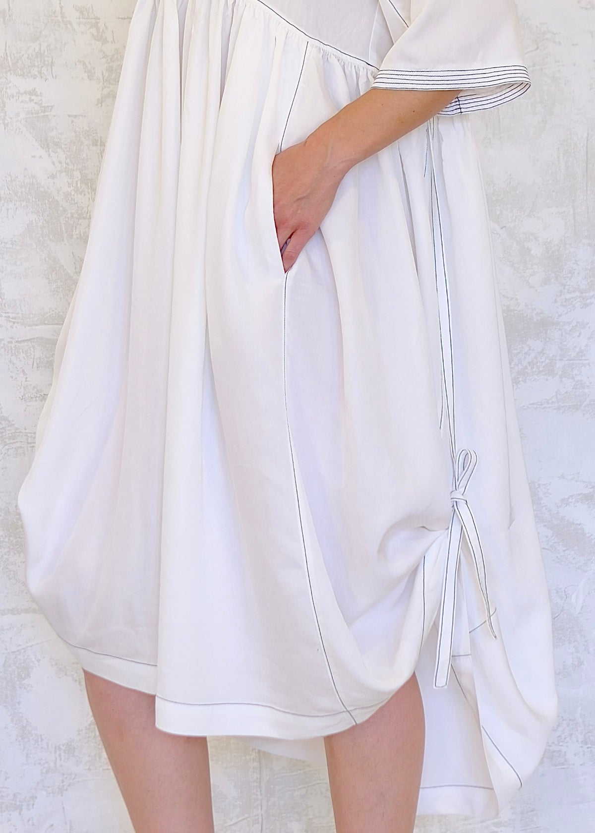 White dress with the hem tied up on one side against a textured white background