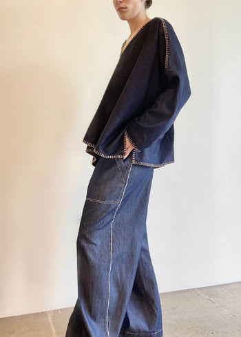 side view of Person wearing a navy blue denim Praia poncho and jeans standing against a plain background