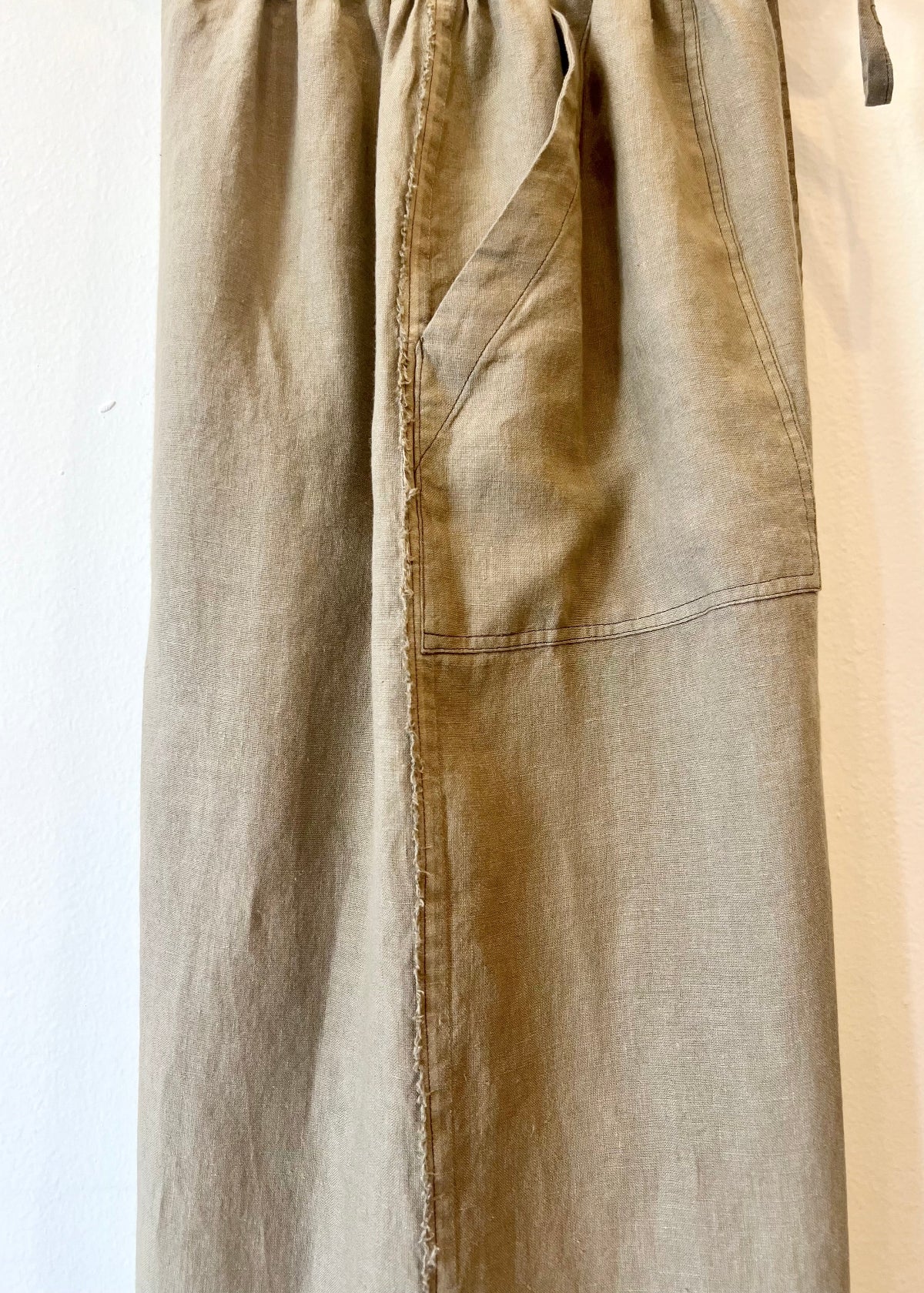 side detail of Beige pants with pocket and frayed edge on a white background